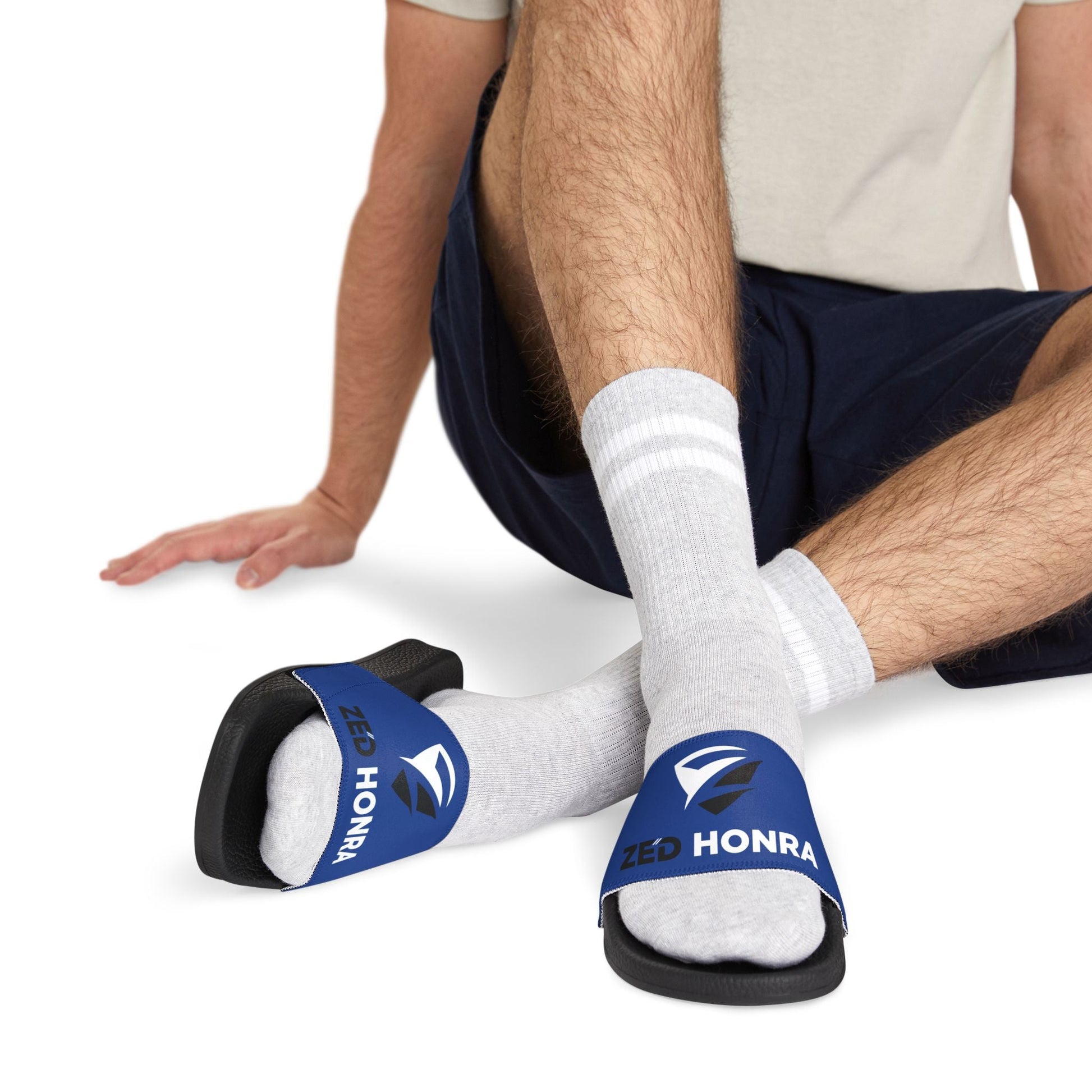 Model wearing blue Zed Honra sandals with white socks, seated on white floor.