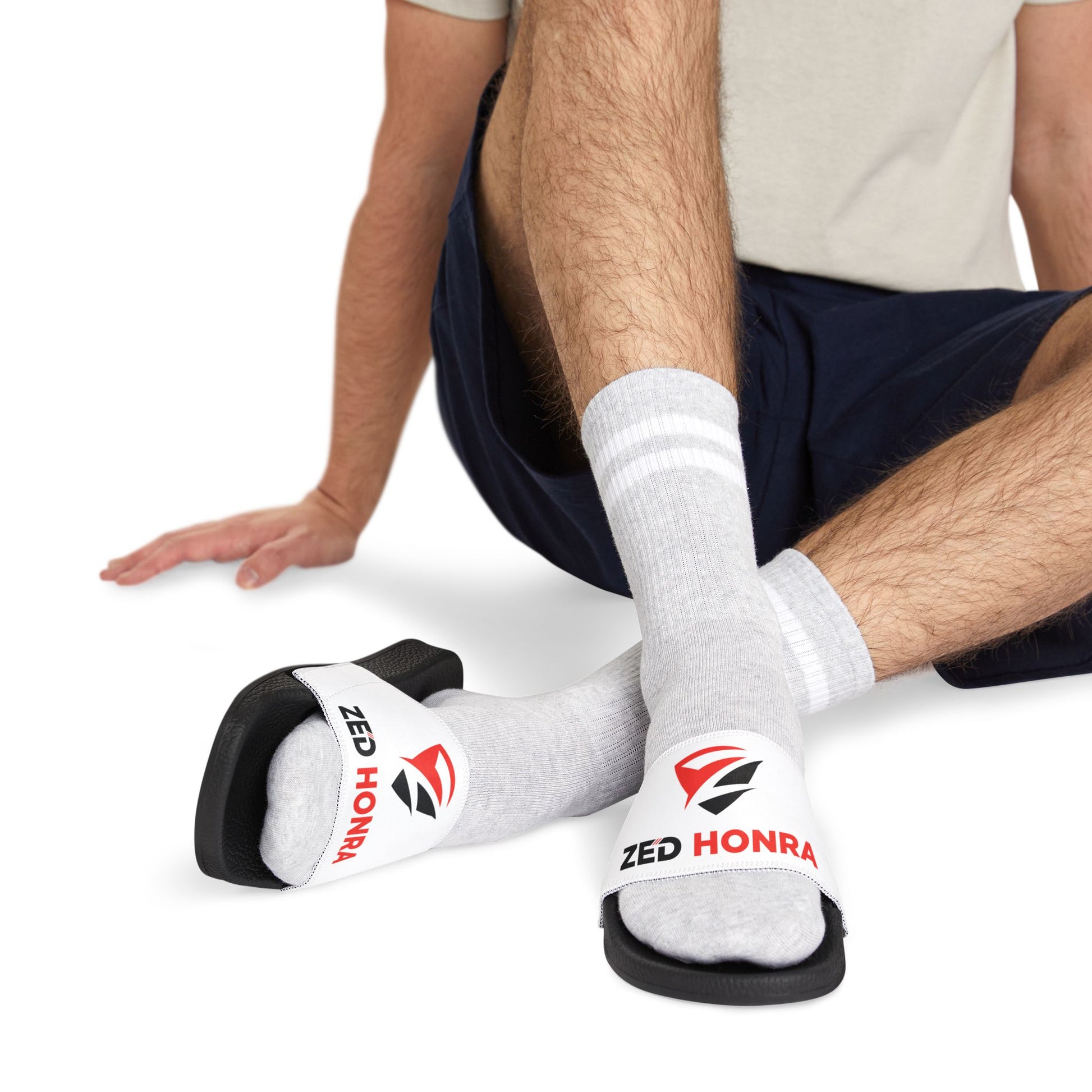 Model standing in white Zed Honra sandals with red logo, paired with socks.